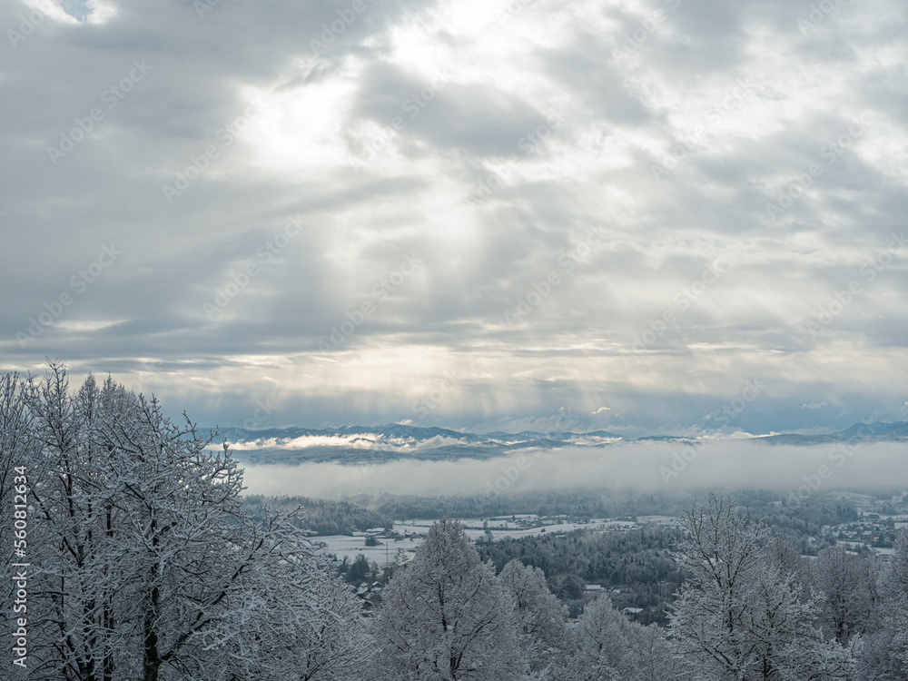 Sun rays shine through receding storm clouds rolling across snowy countryside