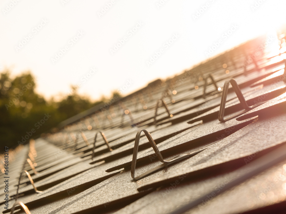 CLOSE UP, DOF: Tiled rooftop with snow guards glowing in golden winter sunlight