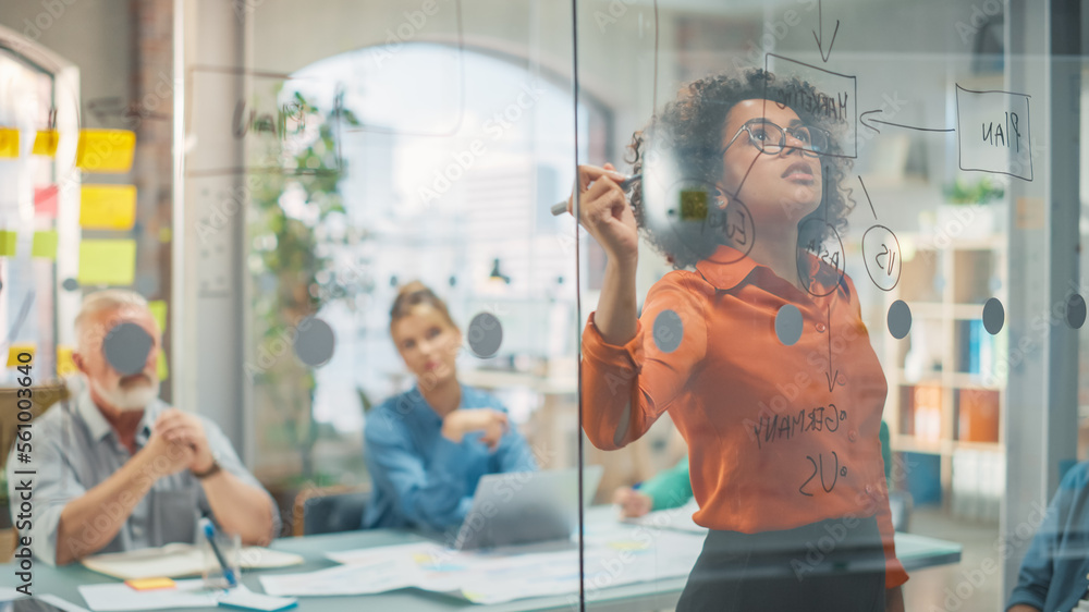 Portrait of Black Female Specialist Writing on Glass Board and Brainstorming with Team in a Stylish 