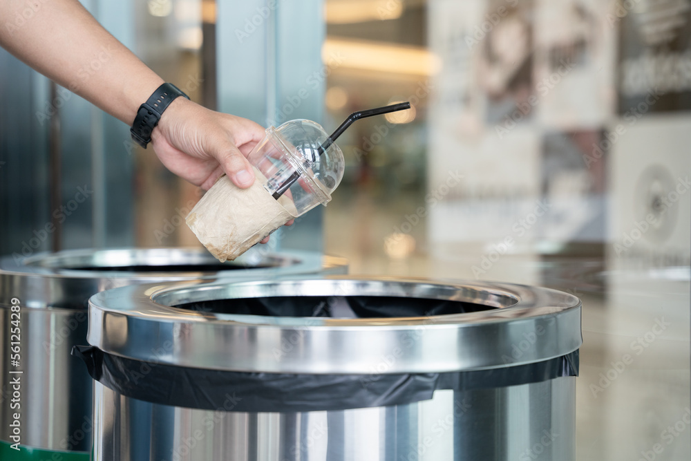 Close-up hand of A man throwing empty plastic coffee mugs cup in recycling bin.