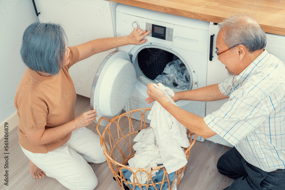 Senior couple working together to complete their household chores at the washing machine in a happy 