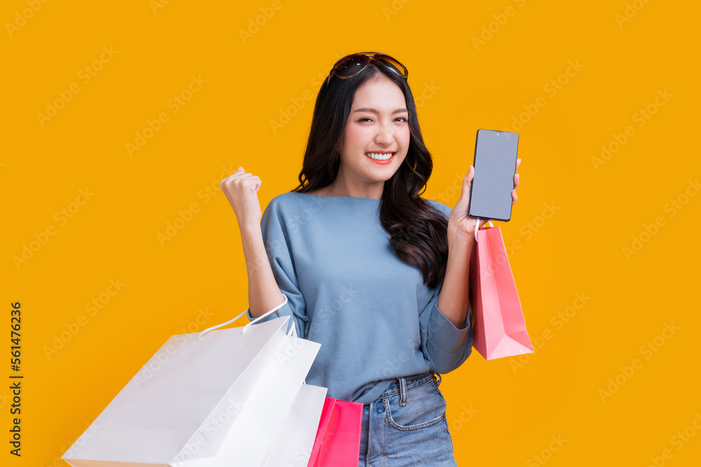 Asian happy female woman girl holds colourful shopping packages   standing on yellow background stud