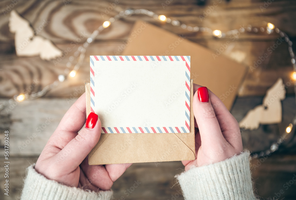 Blank postcard and envelope in female hands on a blurred wooden background.