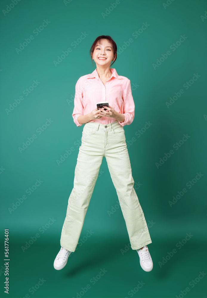 Full length photo of young Asian girl using smartphone on green background