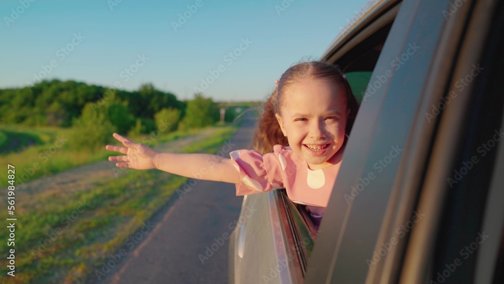 Child, stretching his hand out of car window, laughs. Girl child looks out of car window. Happy fami