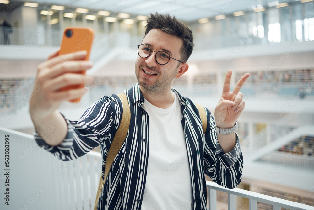 College student, man and library selfie at campus with phone, peace hand and smile on social media. 