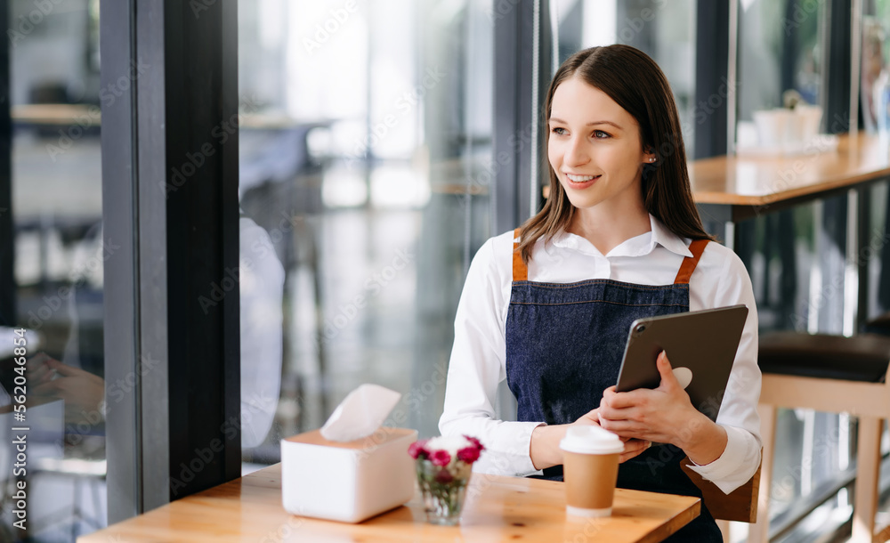 Woman coffee shop owner holding  notepad and digital tablet ready to receive orders.  in cafe restau