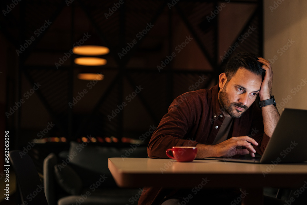 Focused man working on the new project, over the laptop, late at night.