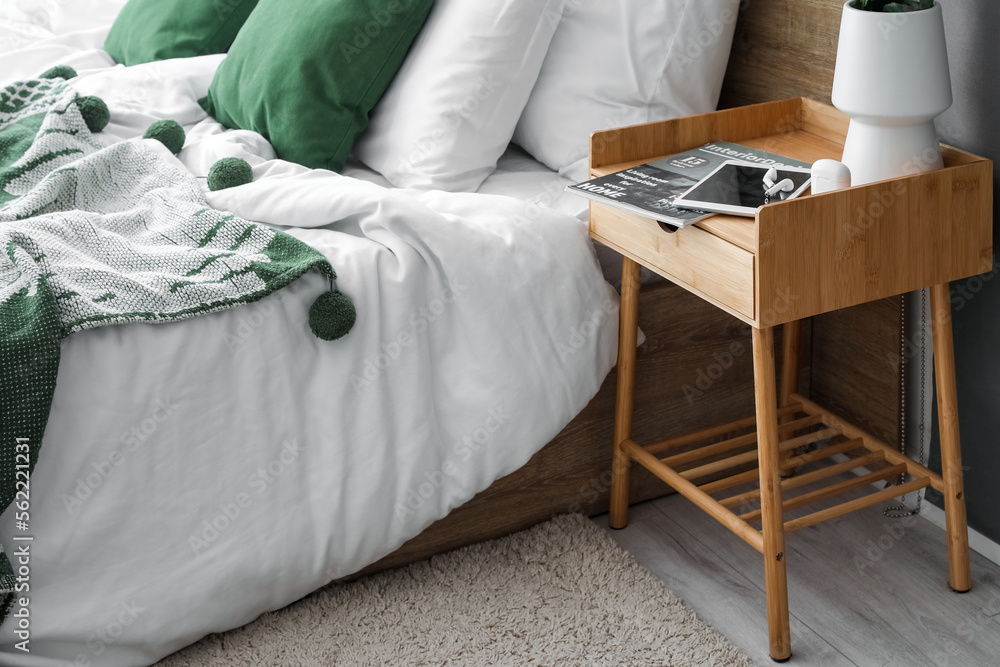 Tablet computer with earphones, magazine and vase on table in bedroom