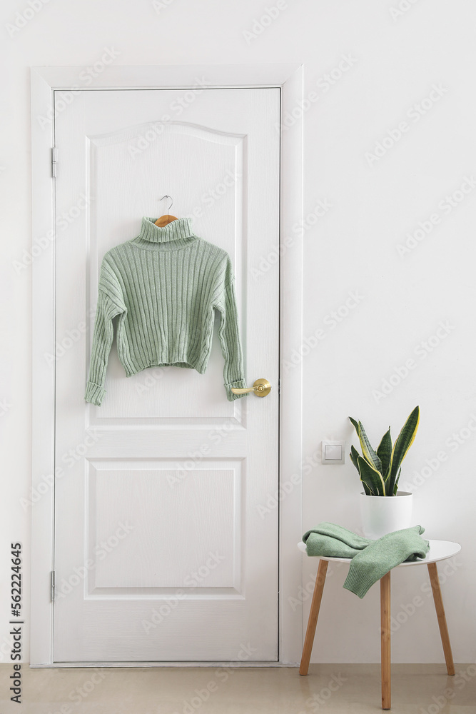 Green sweater hanging on white door in room