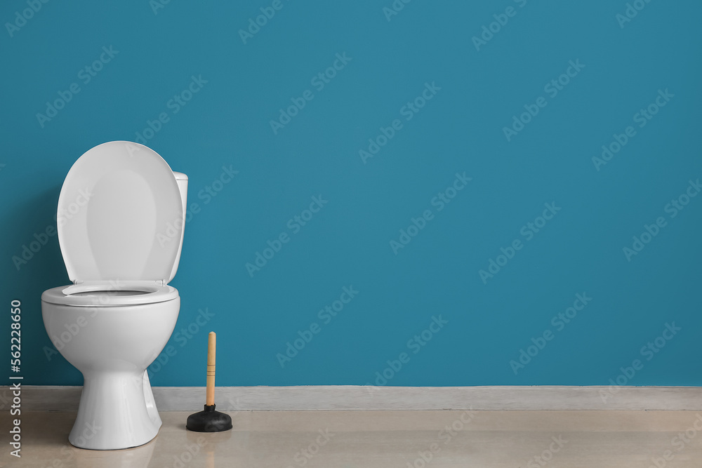 Ceramic toilet bowl and plunger near blue wall