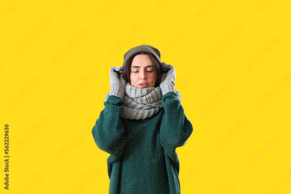 Frozen young woman in winter clothes on yellow background