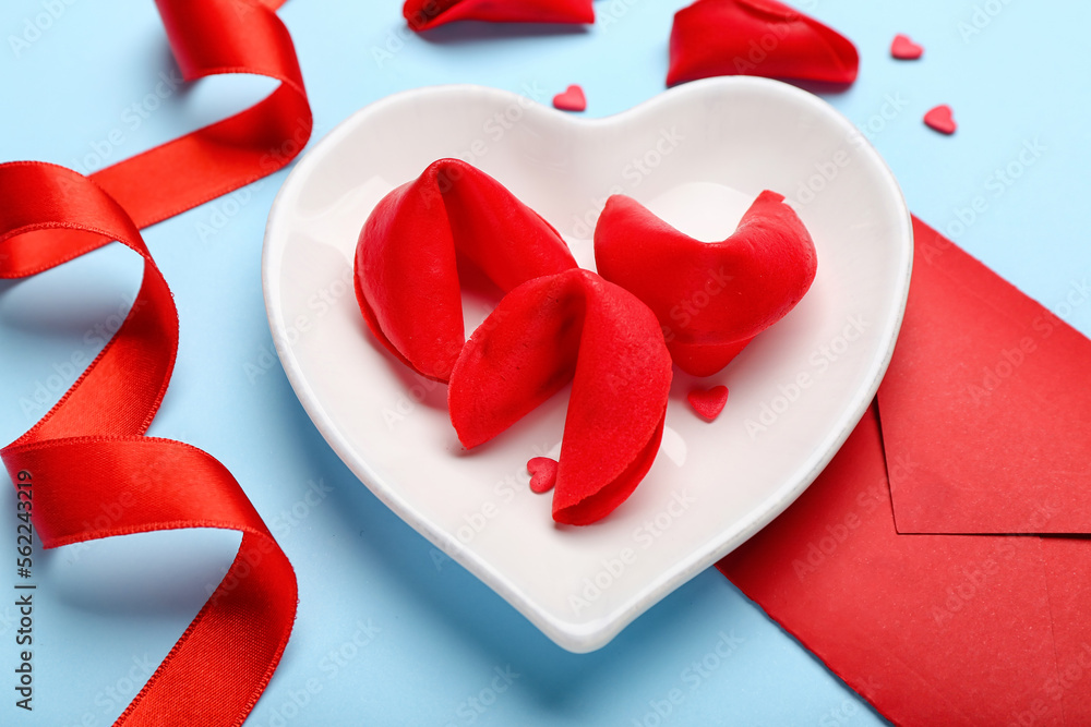 Plate of fortune cookies with envelope and ribbon on blue background, closeup. Valentines Day celeb