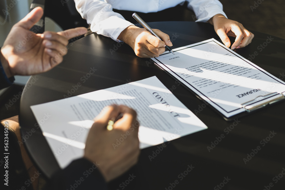 Businessman in suit in his office showing an insurance policy and pointing with a pen where the poli