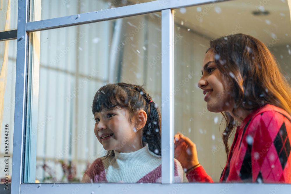 Adorable child looking at the window and admire snowflakes with mother. 