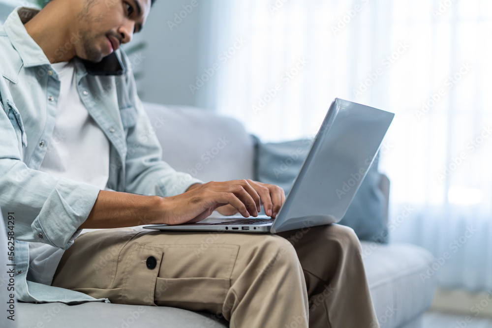 Asian young businessman typing on computer and talking on mobile phone. 