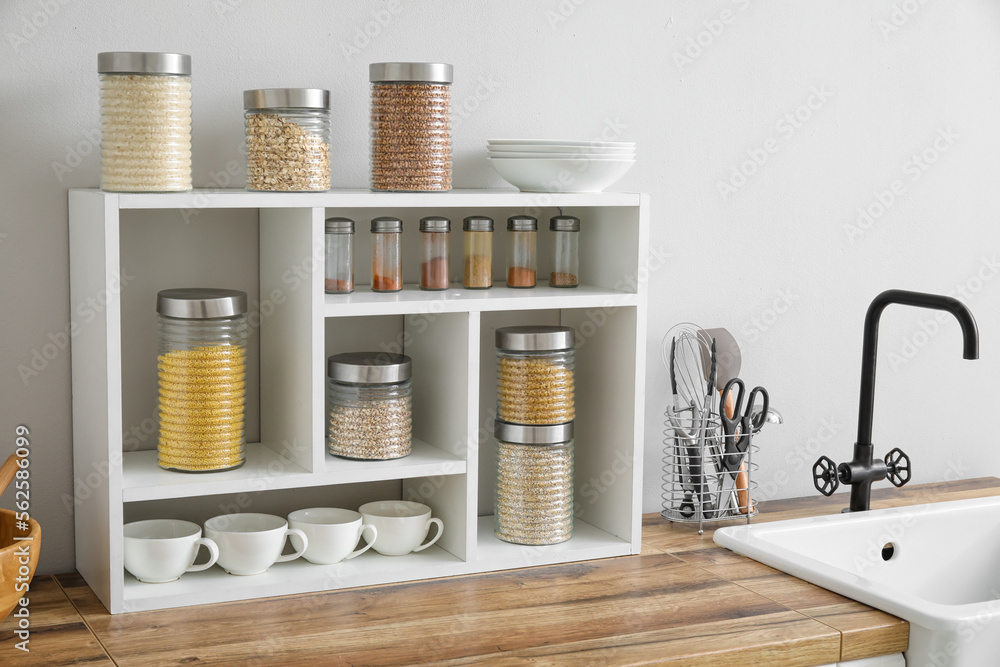 Jars with cereals, spices and utensils on kitchen counter