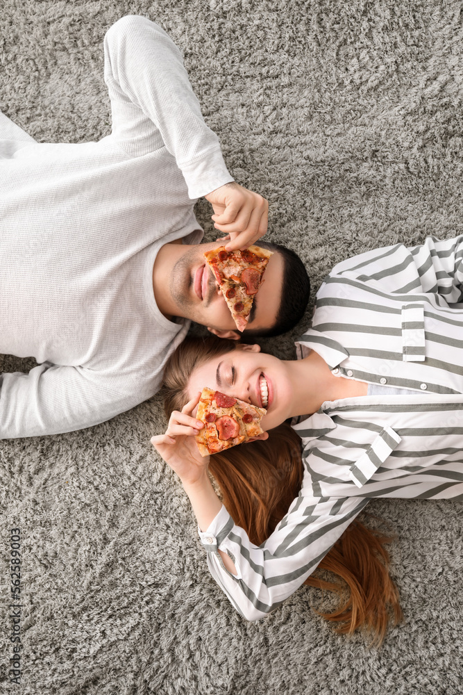 Happy young couple with slices of tasty pizza lying on carpet, top view