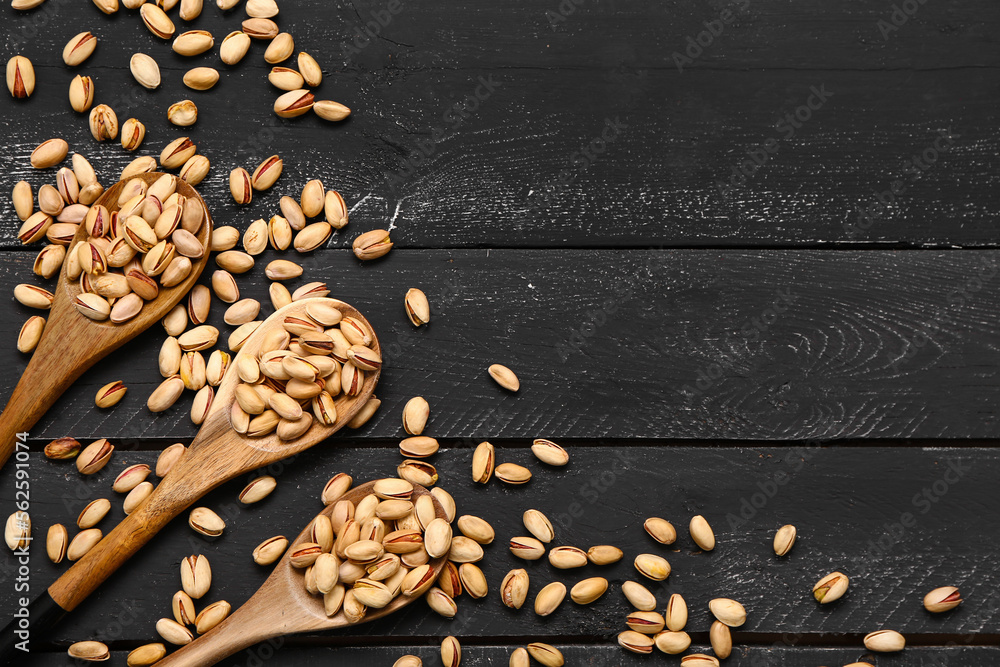 Spoons with tasty pistachios and scattered nuts on black wooden background