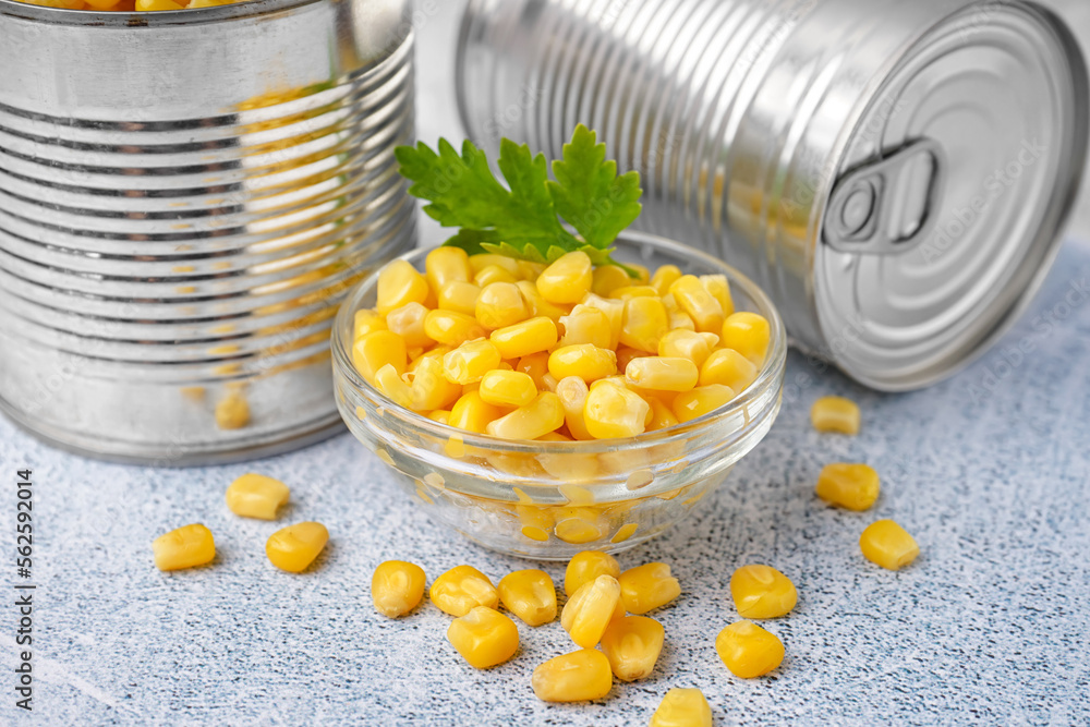 Tin cans, bowl with corn kernels and parsley leaf on grey table