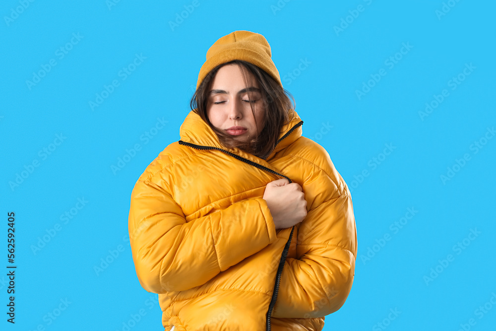 Frozen young woman in winter clothes on blue background