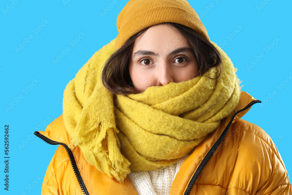 Frozen young woman in winter clothes on blue background, closeup