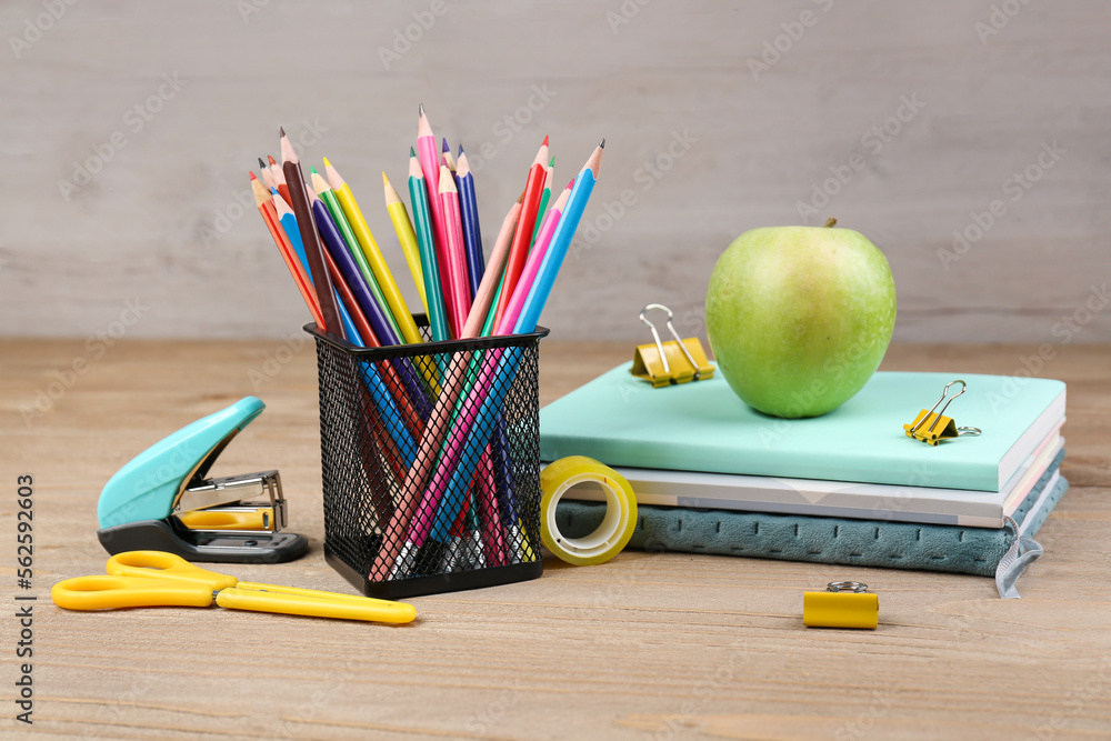 Pencils holder, notebooks with green apple, stapler and scissors on wooden background