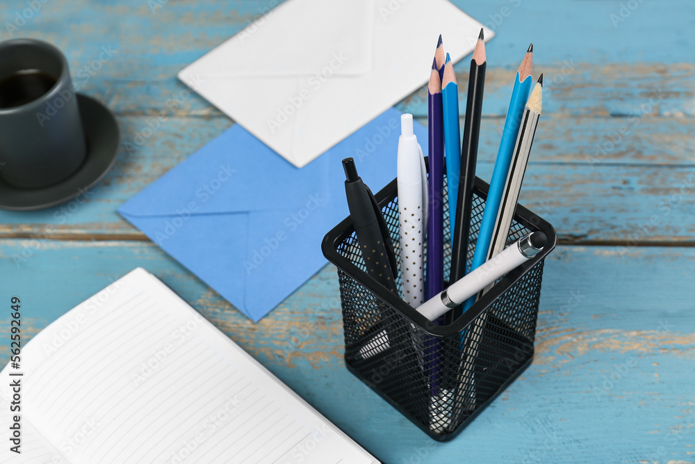 Notebook, envelopes, holder with stationery, cup of coffee and vase with flowers on wooden backgroun