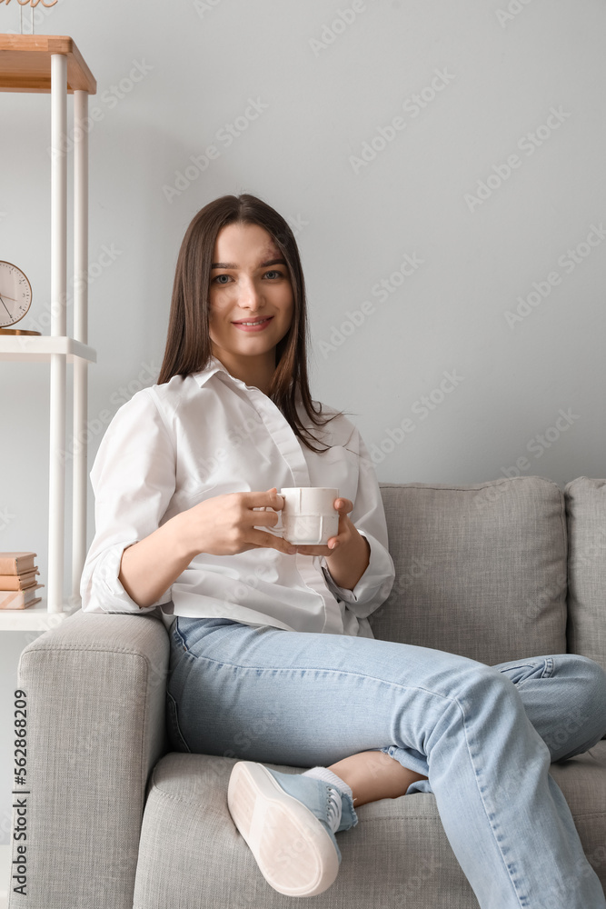 年轻女子拿着一杯热饮坐在家里的沙发上