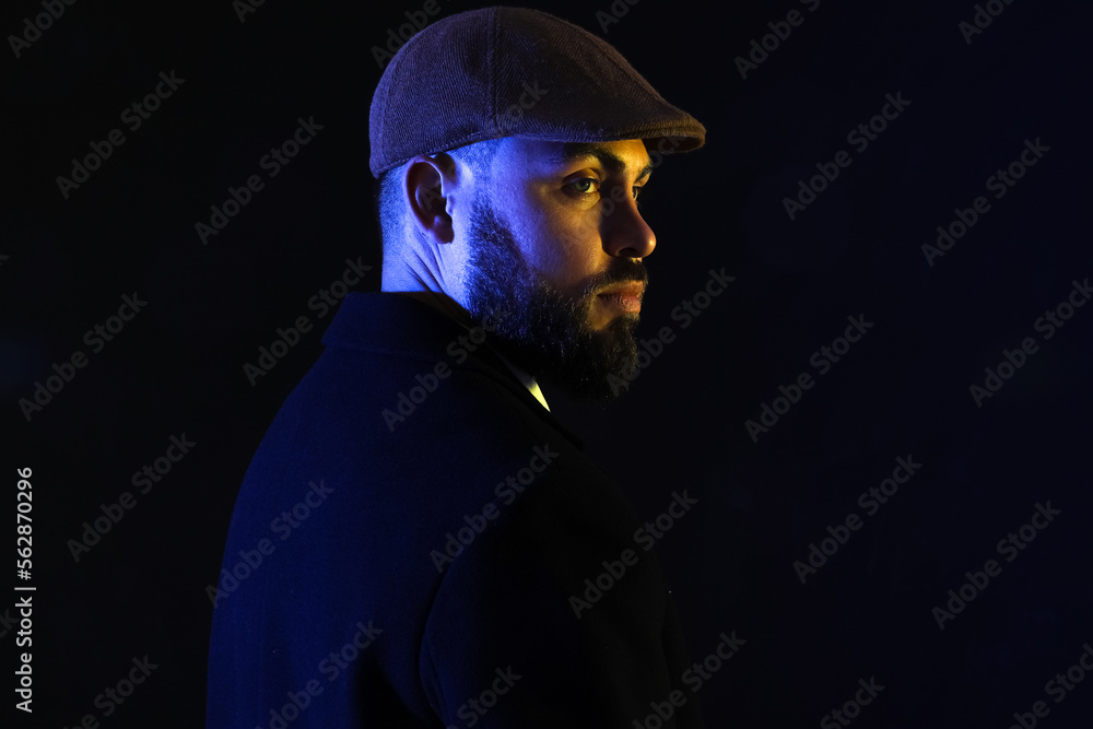 Silhouette of young bearded man in cap on dark background