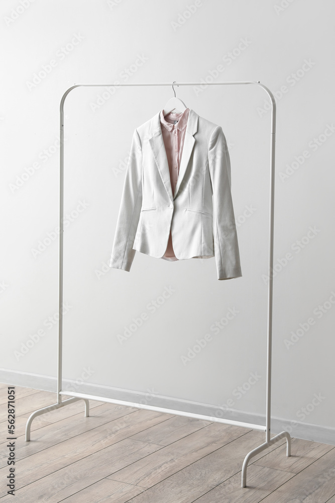 Rack with female jacket and shirt near light wall