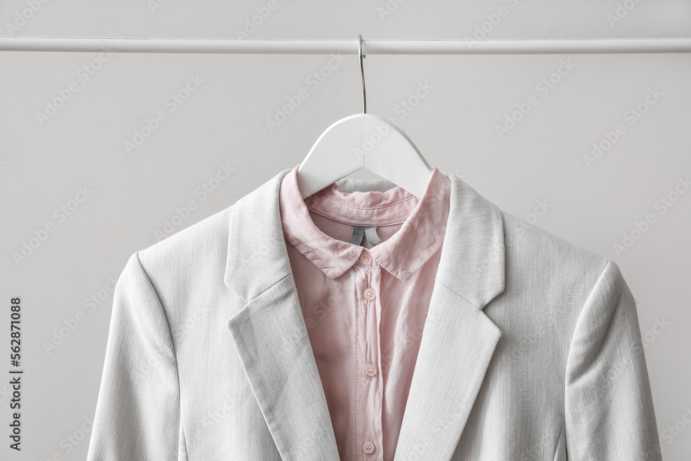 Rack with female jacket and shirt near light wall, closeup