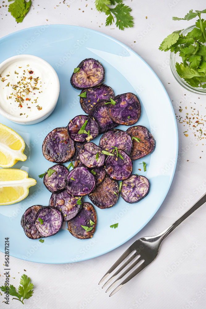 Plate with slices of fried purple potatoes, lemon and sauce on light background, closeup