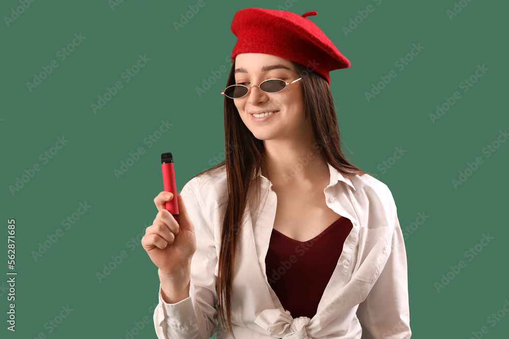 Stylish young woman with disposable electronic cigarette on green background