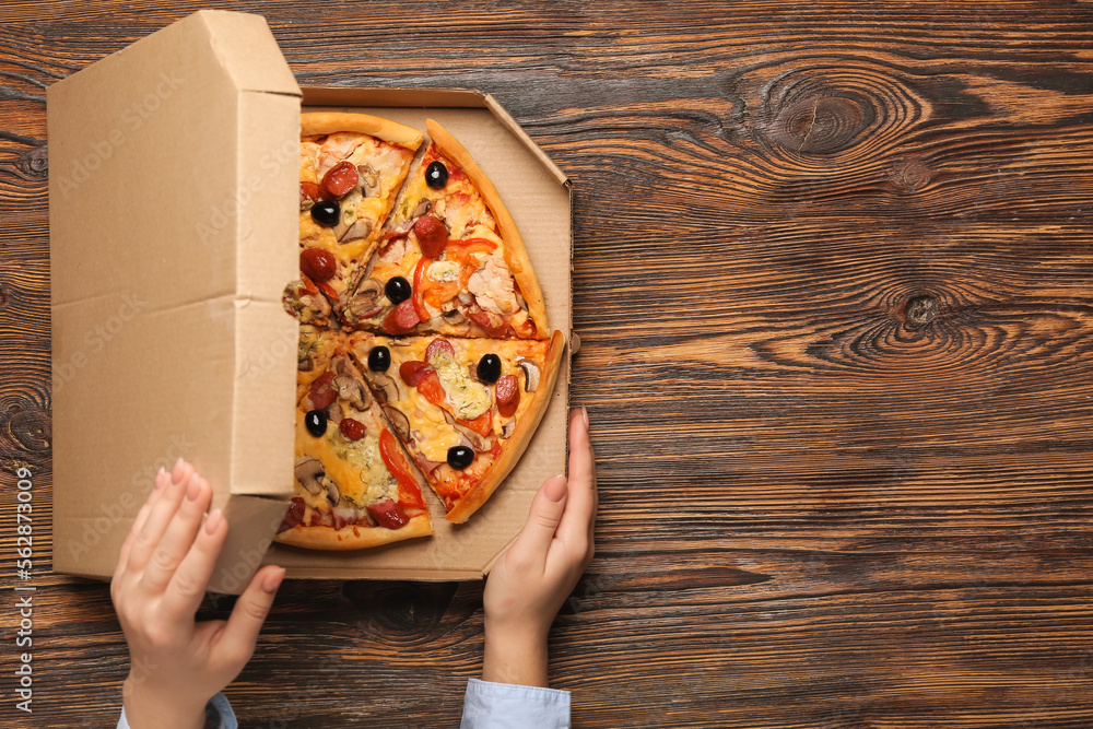 Female hands with box of tasty pizza on wooden background