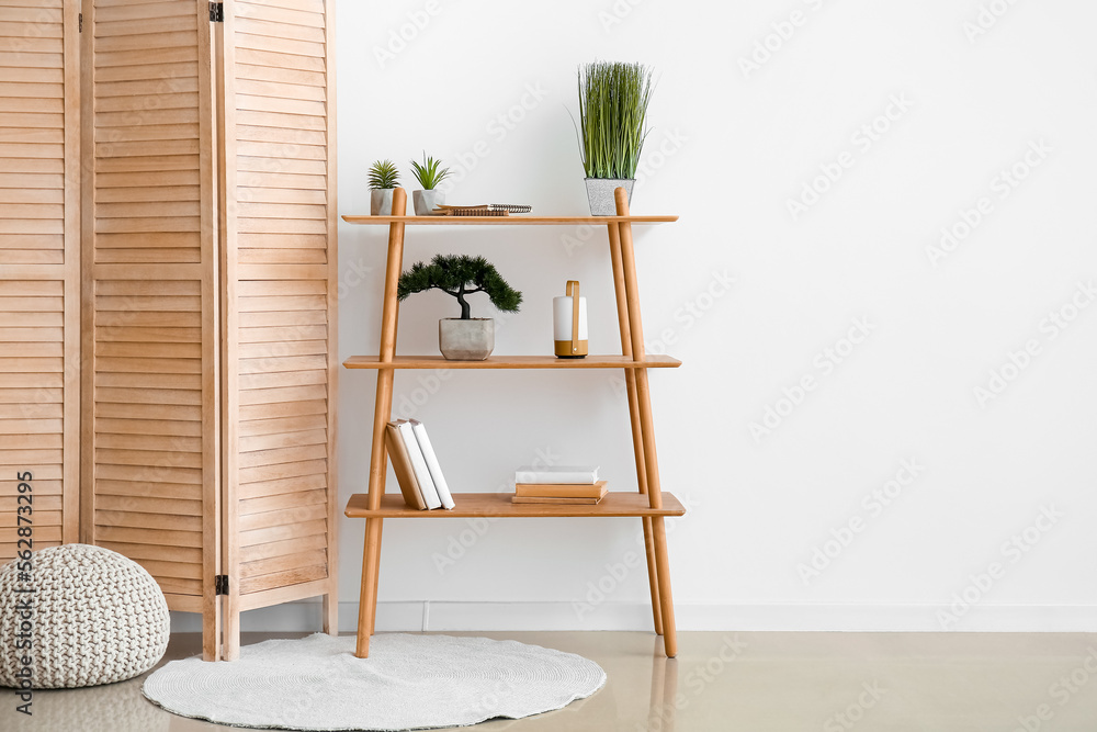 Interior of room with folding screen, shelving unit and pouf near white wall