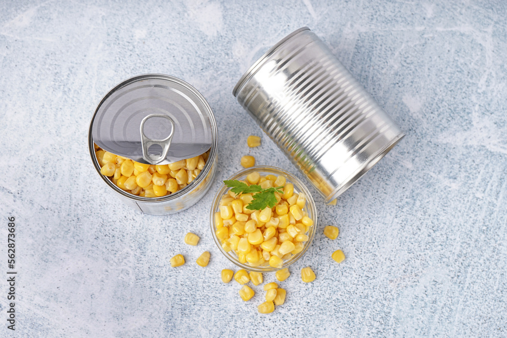 Tin cans, bowl with corn kernels and parsley leaf on grey table