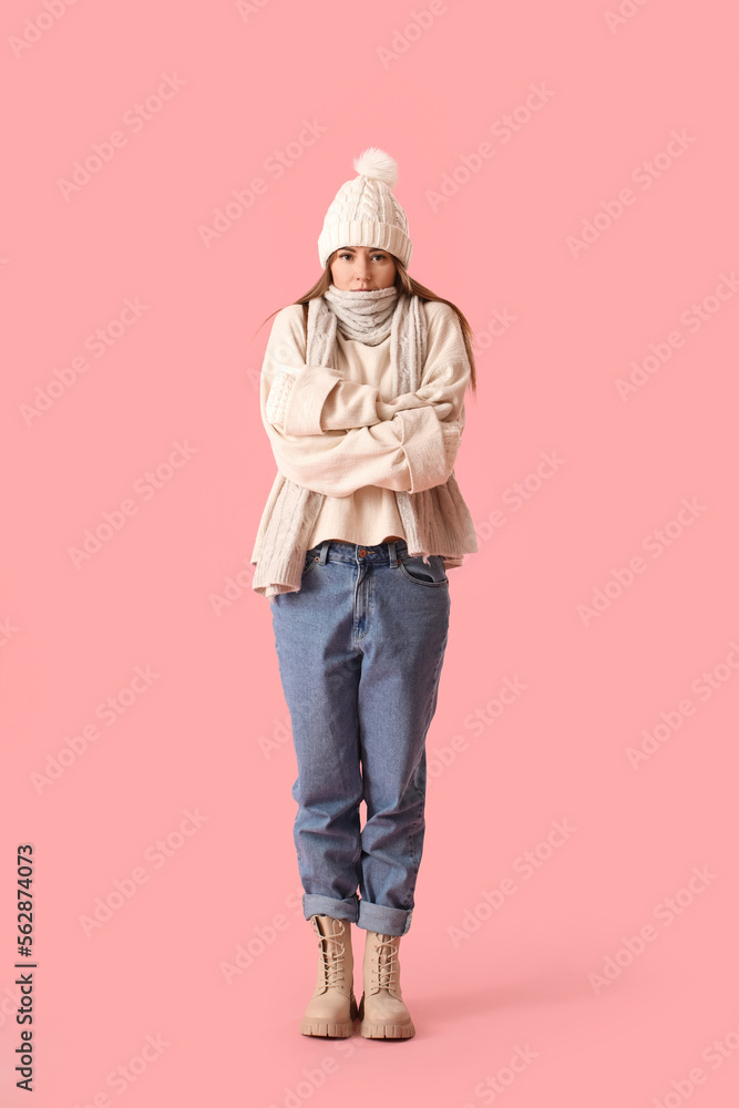 Frozen young woman in winter clothes on pink background