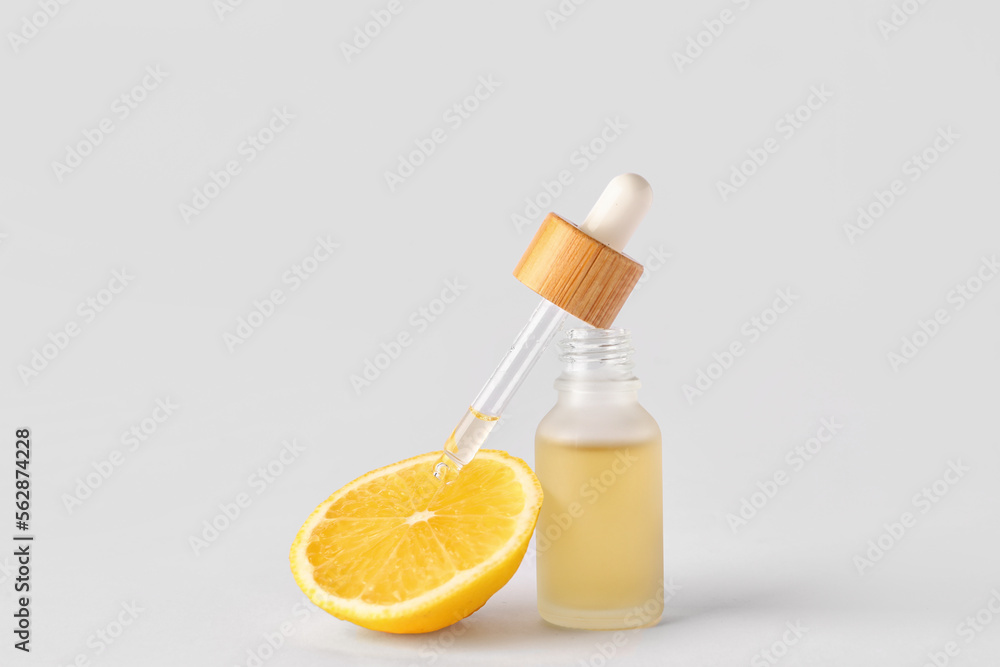 Bottle of serum with lemon on light background