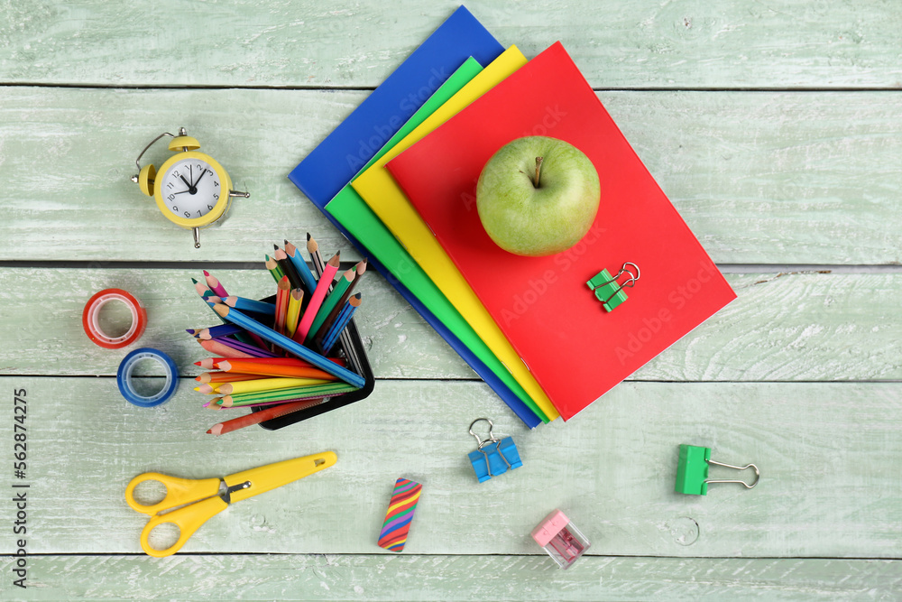 Green apple with notebooks, pencils holder, different stationery and clock on wooden background