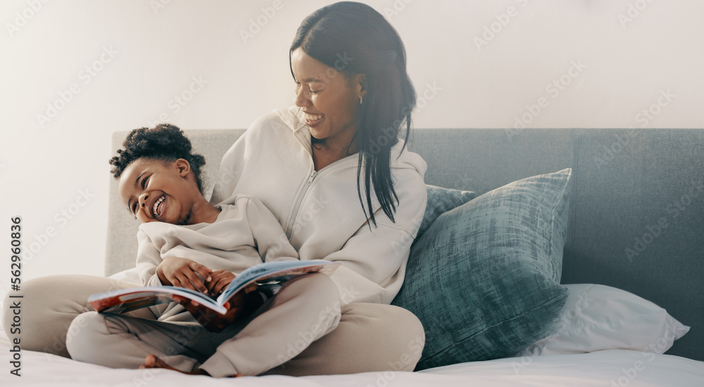 Preschool age girl laughs happily while sitting with her mom reading a story book