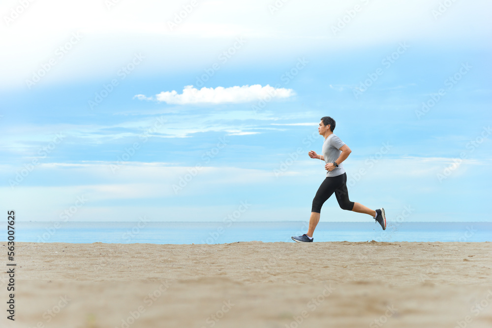 Asian man jogging  on tropical sandy beach with blue sea and clear sky background.