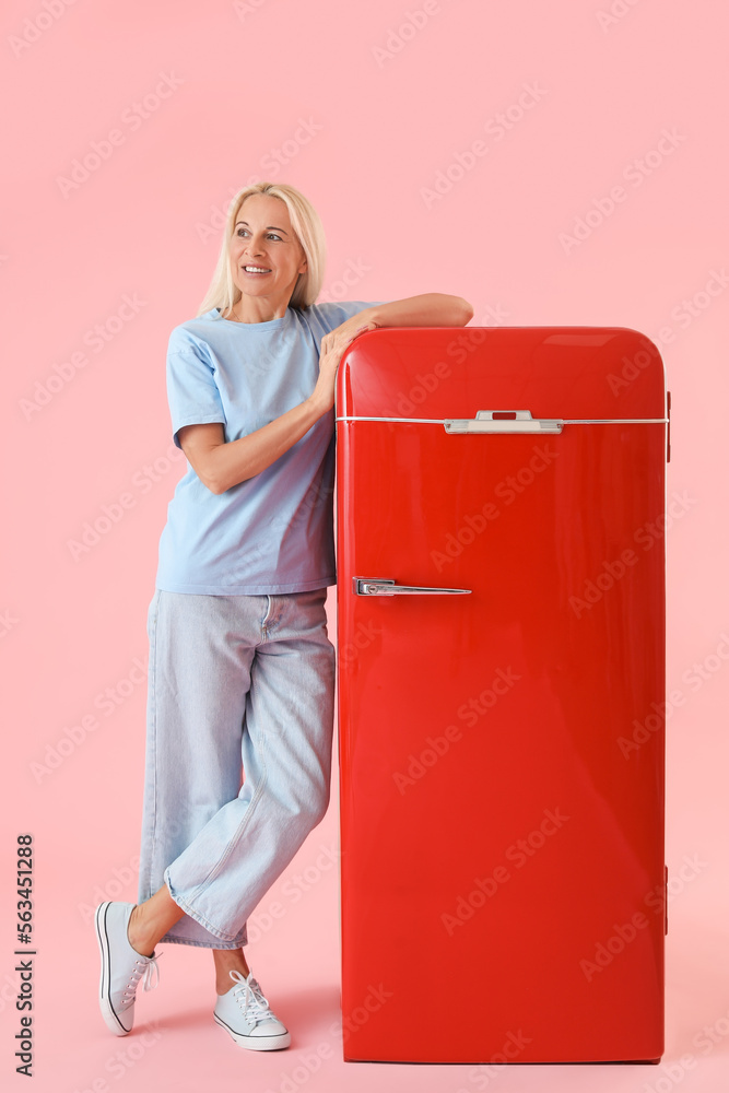 Mature blonde woman with retro fridge on pink background