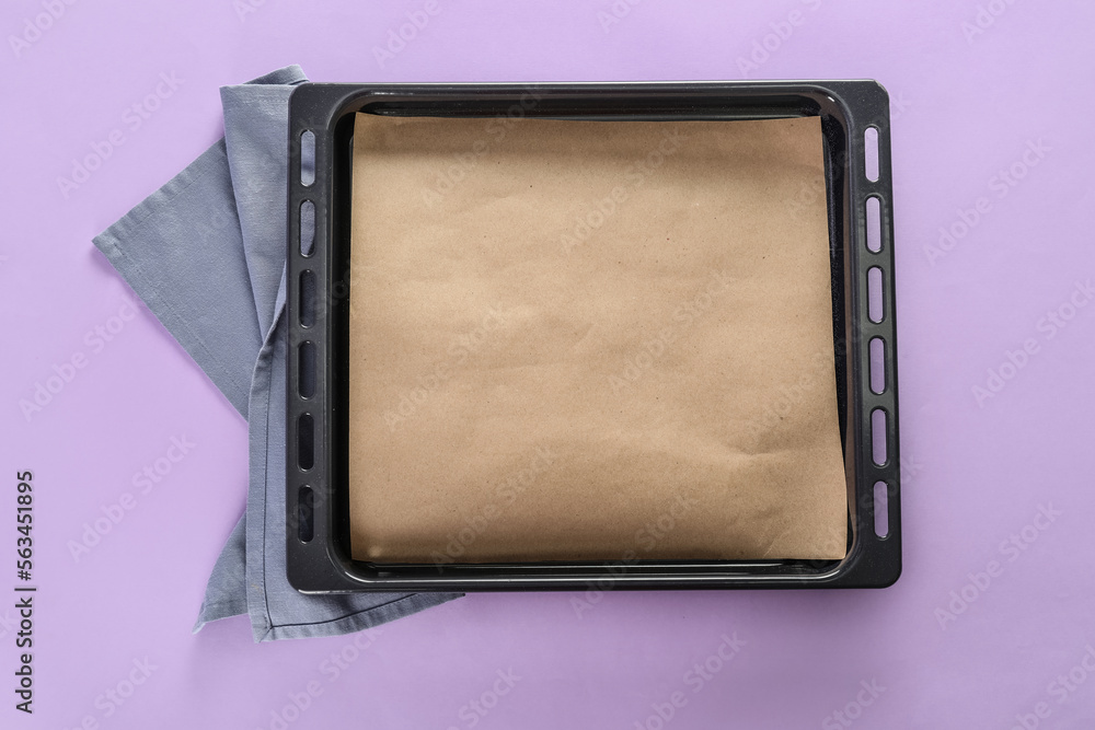 Baking tray with parchment paper and napkin on lilac background