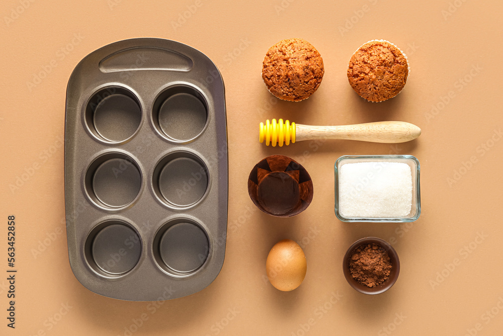 Baking tray with muffins, honey dipper and ingredients on beige background