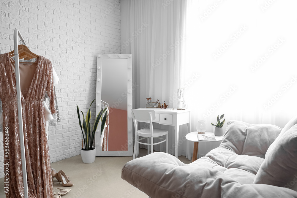 Interior of stylish dressing room with table, mirror and clothes