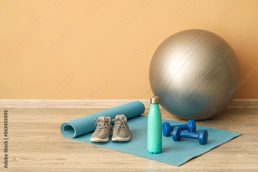 Sports water bottle with equipment and sneakers on mat near beige wall