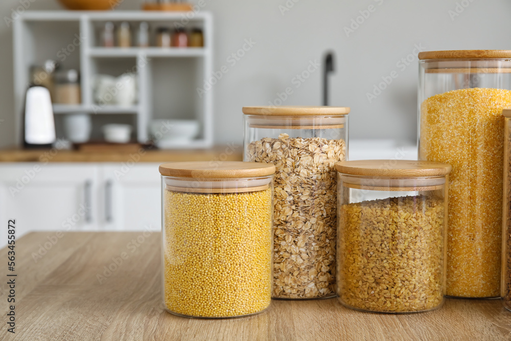 Glass jars with different cereals on wooden table in kitchen, closeup