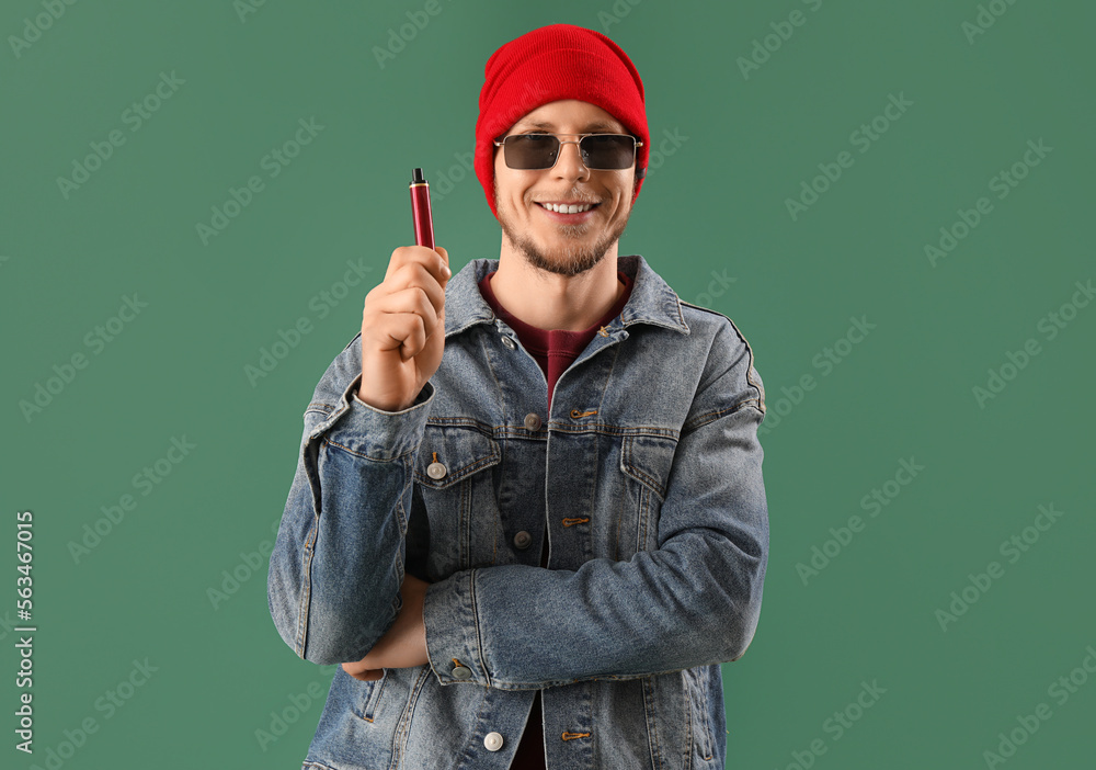 Stylish young man with disposable electronic cigarette on green background