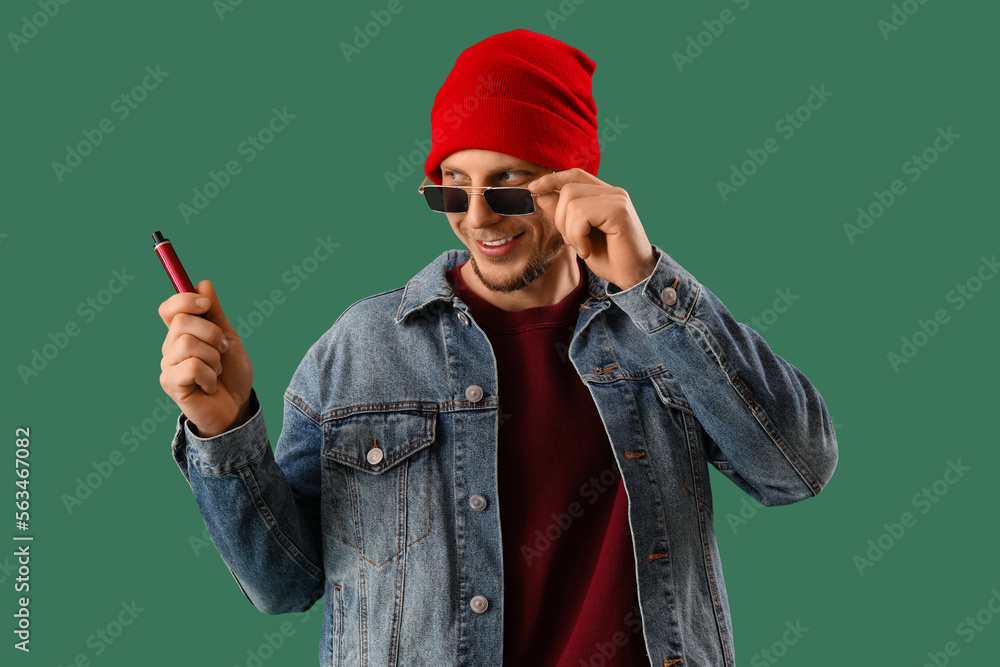 Stylish young man with disposable electronic cigarette on green background